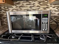 Front view of stainless Hamilton Beach microwave on stovetop showing control panel and display