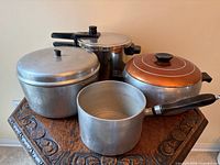 Four pieces of cookware: pressure cooker, two lidded pots, one saucepan