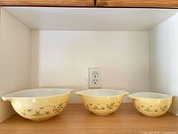 Three Pyrex yellow floral nesting bowls displayed side by side by size