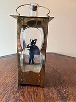 Front view of brass-framed glass musical decanter showing silhouette and stopper