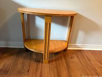 Front view of wooden demilune table showing top surface, lower shelf and decorative central leg