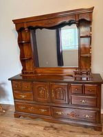 Front view showing dresser base with drawers, cabinet doors, carved details, brass hardware, and attached mirror with side shelves