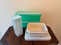 Group of five Tupperware containers: two green keepers stacked, tall translucent cracker keeper, beige container without lid, translucent Square-A-Way container with lid