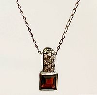 Front view of necklace displaying pendant with garnet and diamonds