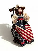 Front view of doll seated in rocking chair holding flag