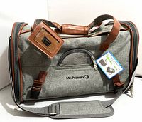 Front view of grey Mr. Peanut's pet carrier with tag attached, showing handles, front pocket, shoulder strap