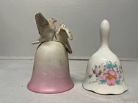 Front view of both ceramic bells showing bird-topped pink bell and floral white bell