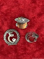 Front view of all three sterling silver brooches on red fabric