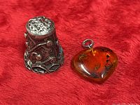 Sterling silver thimble and amber heart pendant side by side on red fabric
