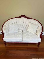 Front view of carved wood loveseat with two matching pillows