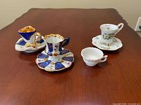 Front view of four miniature porcelain teacups with three saucers displayed on table