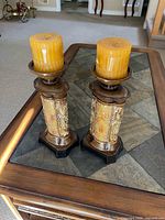 Pair of candle holders with amber pillar candles on table, showing design and condition