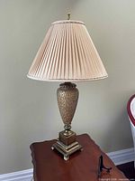Bronze-tone table lamp with pleated beige shade on wooden table