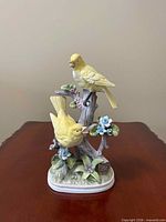 front view showing both yellow birds, branch, leaves, flowers