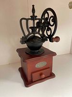 Front view of manual coffee grinder showing wooden base, Café plaque, drawer and cast iron mechanism with hand crank wheel