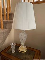 Full view of one crystal table lamp with shade and matching glass holder on wooden table