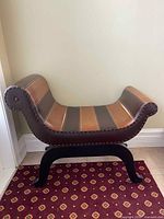 Side view of bench showing striped leather upholstery, curved seat, and nailhead trim