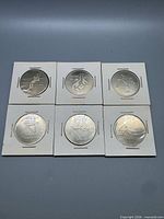 Front view of six Olympic Trust coins in flips