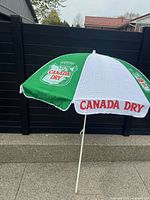 Umbrella fully opened showing green and white panels with Canada Dry logos