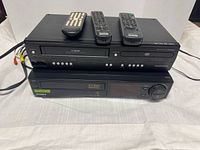 Magnavox combo unit stacked on Sony VCR with cables and three remotes on top