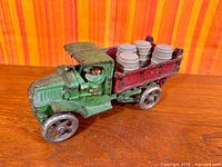 Full view of green and red cast iron dump truck with barrels in bed