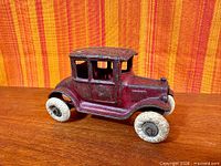 Left front quarter view of red cast iron Ford Model T toy car on wood surface