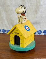 Full view of Snoopy Flying Ace wooden music box on teal base
