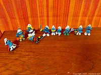 All eight Smurf figurines lined on wooden surface