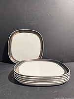 stack of six square white saucers with black rim, one propped upright