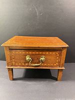 Front view showing brass handle, inlay detail, legs