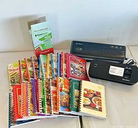 Overall lot showing two FoodSaver sealers, roll box, and array of cookbooks