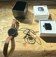 Round-faced watch with leather strap, charging cable, empty box, extra module in box