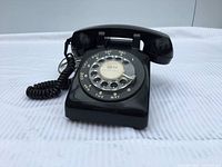 Three-quarter view of black rotary telephone showing handset, dial and cords
