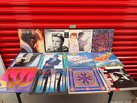 All 12 album covers laid out on table against red backdrop
