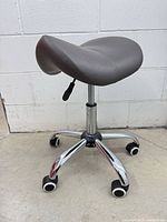 Full view of grey saddle stool showing seat, base and casters