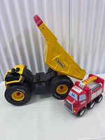 Tonka dump truck with bed raised beside Little Tikes fire truck