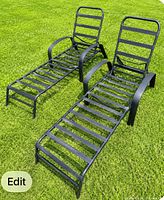 Two black metal slatted chaise lounges on grass, showing overall design and condition