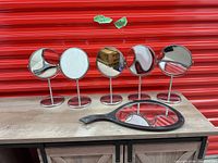 Five round tabletop mirrors and one handheld mirror displayed on wooden surface