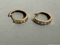 Pair of gold hoop earrings side by side showing front view with stones