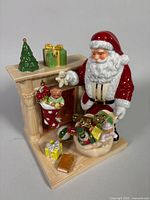 Front angled view of Santa’s Surprise figurine showing fireplace, Santa, stocking and gifts