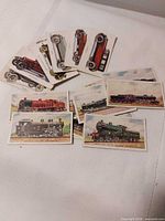 Pile of illustrated cigarette cards showing automobiles and trains