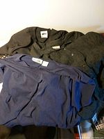 Three garments laid flat: black dress, textured black jacket, navy top