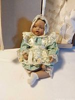 Front view of baby doll seated showing dress, bonnet and one sock off