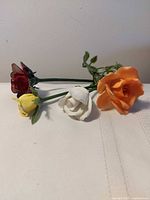 Group of four porcelain roses in red, yellow, white, orange on wire stems