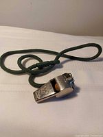 Whistle with green lanyard coiled on white surface