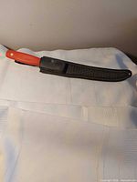 Knife with orange handle partially in black sheath on white background
