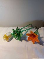 Three long stem glass flowers laid on white surface