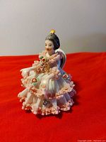 Front view of seated Dresden figurine showing lace dress and applied flowers