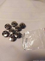 Eight metal bobbins and bag with needles on white surface