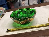 Side profile of green glass bowl showing gold accents and tape measure for scale